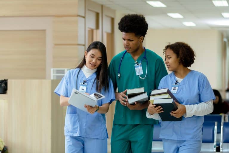 It's a picture of three nursing students walking at the university and looking at some books studying for the NCLEX